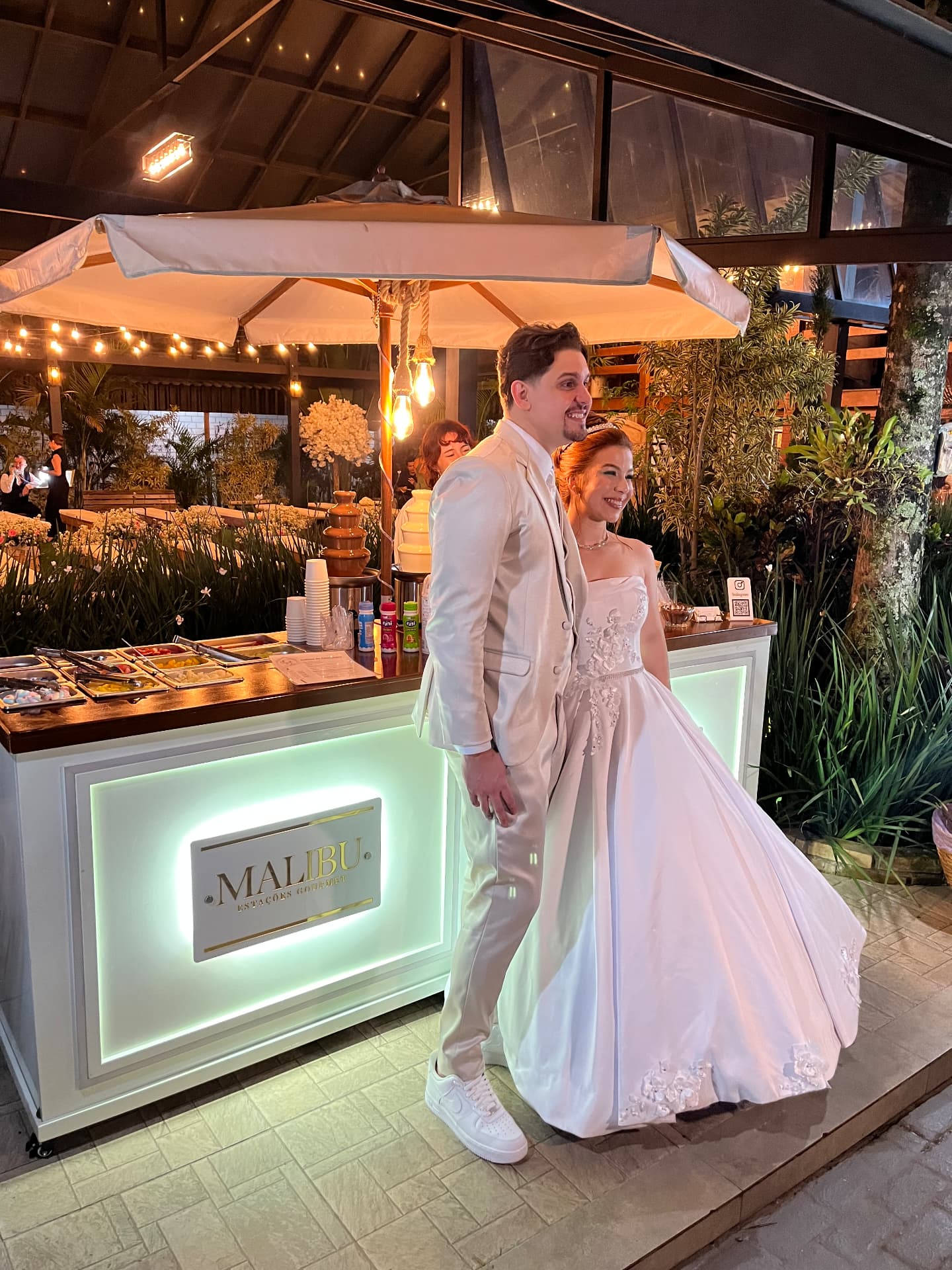 Noivos ao lado da estação gourmet iluminada da Malibu Estações Gourmet em casamento